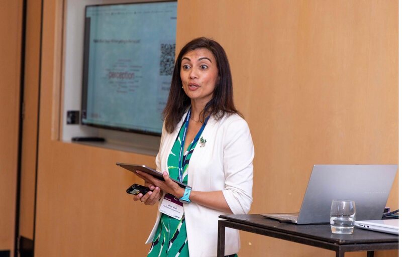 Devi Virdi speaking on stage with presentation screen